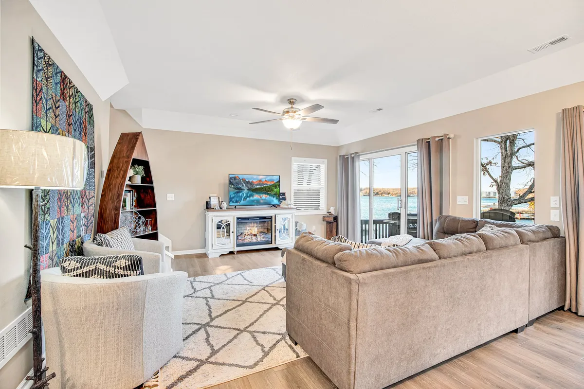 A spacious, sunlit living room with a large sectional sofa arranged for group relaxation, contemporary artwork on the wall, a television for entertainment, and wide windows providing scenic views of the lake. The setting feels both cozy and inviting, ideal for unwinding after a day of adventure or spending quality time together.