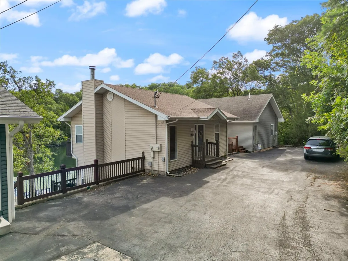 The exterior view showcases the house facade, driveway, and the surrounding greenery, presenting a serene, well-maintained environment. The entrance and surrounding space evoke a sense of safety and comfort for arriving guests.