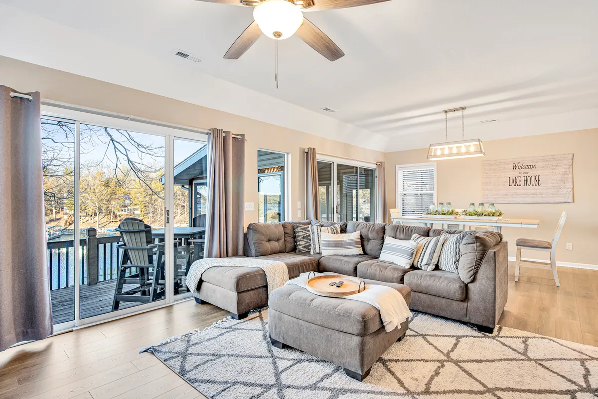 A cozy living room with a comfortable sofa arranged by large windows that look out onto sunset views. The adjacent dining area is visible, creating a sense of openness and connection between multiple gathering spaces.