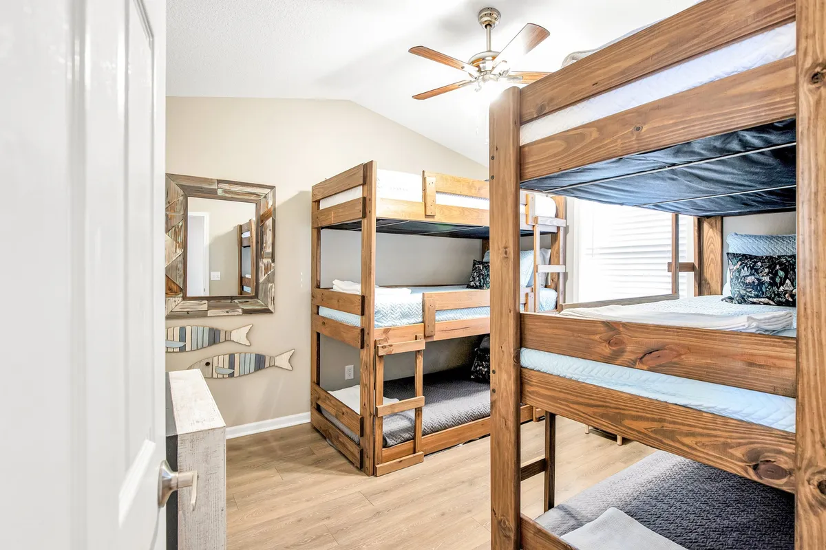 A cozy, inviting bedroom featuring triple bunk beds, wooden accents, and a decorative mirror. The arrangement suggests a family-friendly environment perfect for children or groups, with playful yet comfortable bedding and warm lighting.