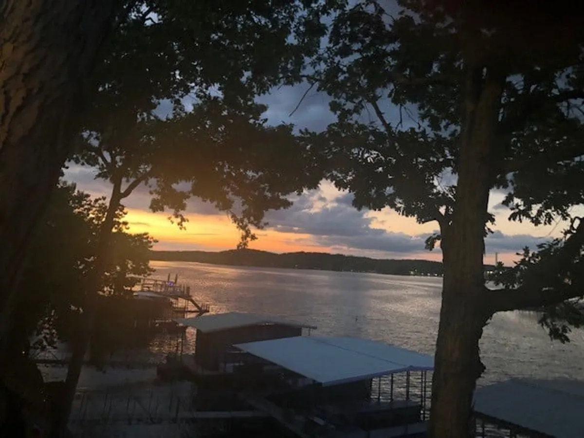 A stunning view of the lake at sunset, framed by trees and lively docks. The mood is tranquil and memorable, with hints of ongoing water activities like boating and fishing, and the setting sun casting a golden glow over the water.