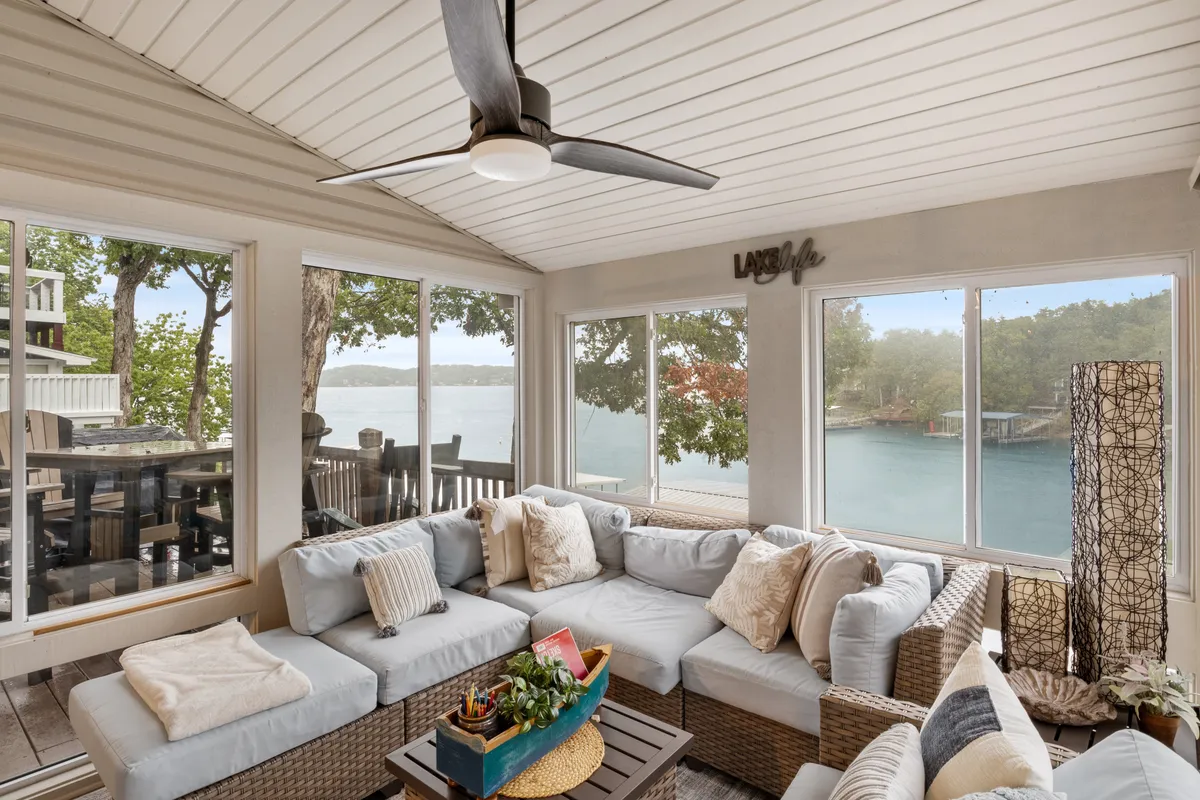 A comfortable and elegantly decorated living room with a large sectional sofa and coffee table adorned with plants. Through expansive windows, there is a stunning view of the lake, bringing in abundant natural light and offering a seamless blend of indoor comfort and outdoor beauty.