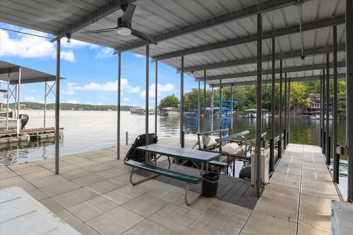 An inviting view of a dock extending over the water, with fishing boats moored nearby and a picnic table set up for lakeside meals. The gentle water glimmers under open sky, hinting at leisurely afternoons and memorable outings.